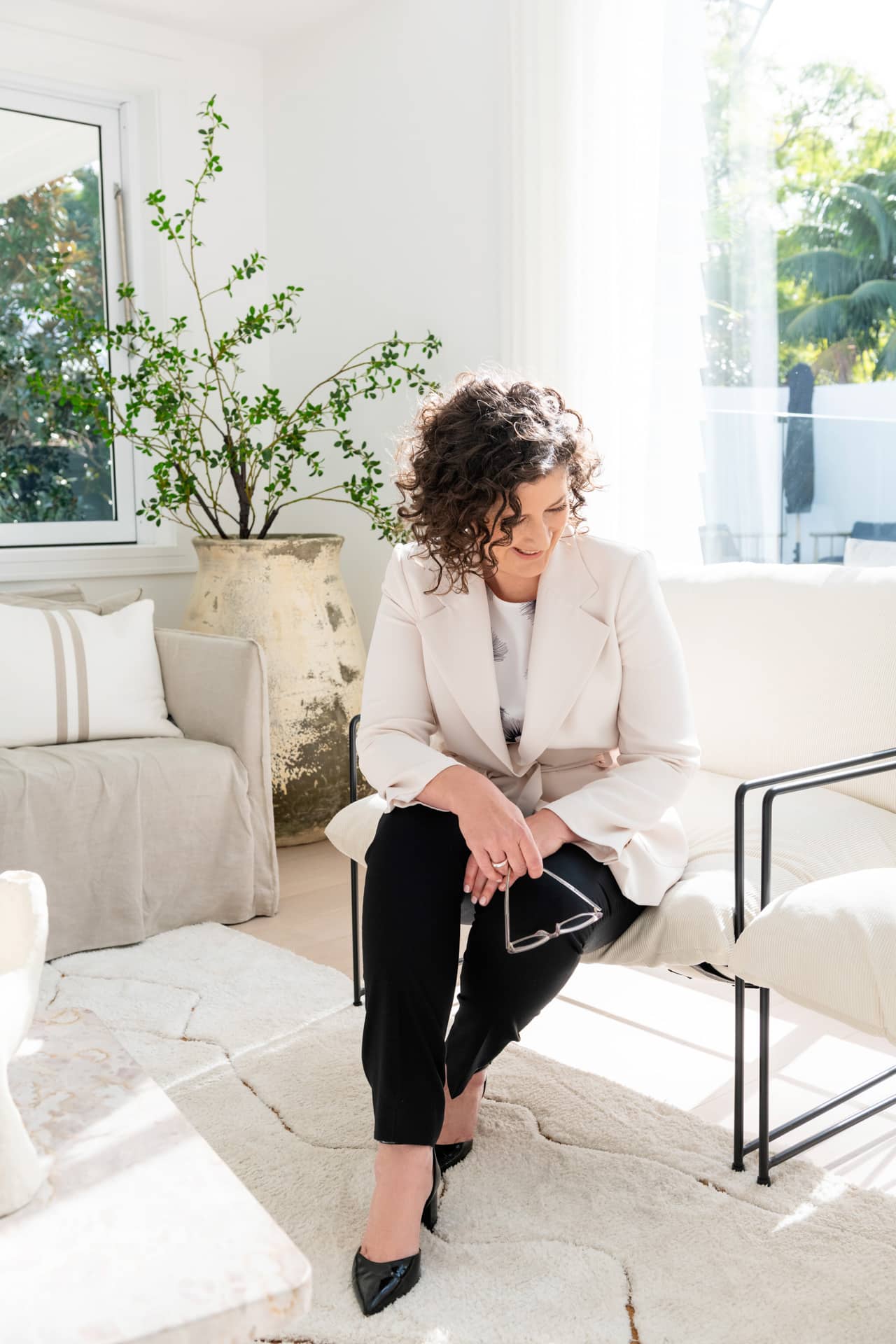Marnie Cooper Mediator and Separation Strategist sits on an off-white sofa in a sun lit room in Sydney.